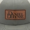Grey trucker hat with a mesh back and a leather patch with the Daniel Defense logo